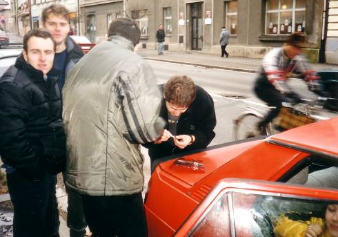 foto č. 001 - Před odjezdem z Kolína. Michal lepí světlo k autu, David mu radí a Martin s Tomášem mlčky přihlížejí.
